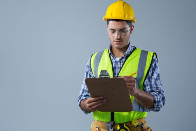 man-in-hardhat-and-safety-vest-writing-on-clipboard