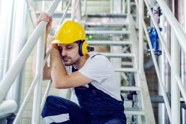tired-worker-in protective-gear-leaning-against-stairway-railing-sleeping