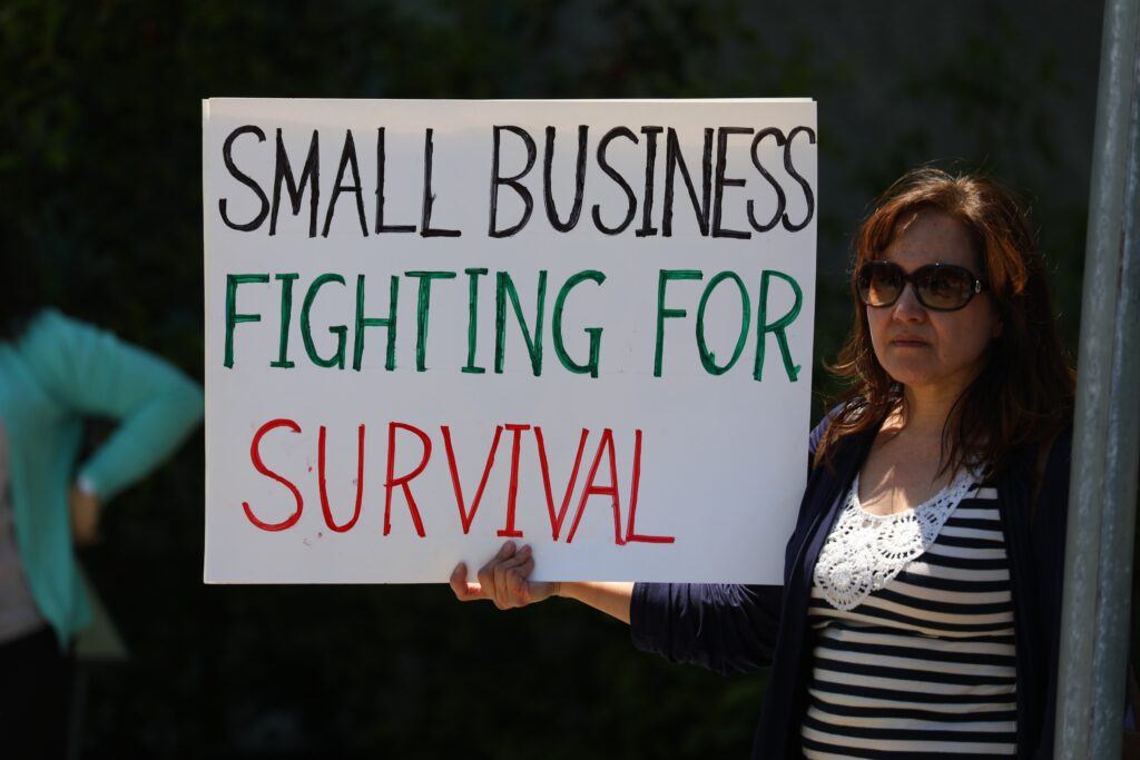 woman holding a sign reading Small Business Fighting for Survival